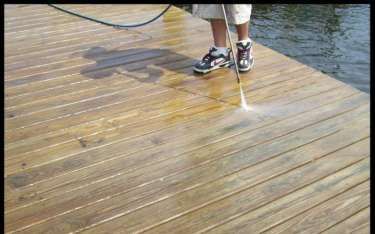 Person power washing a wooden dock next to the water.