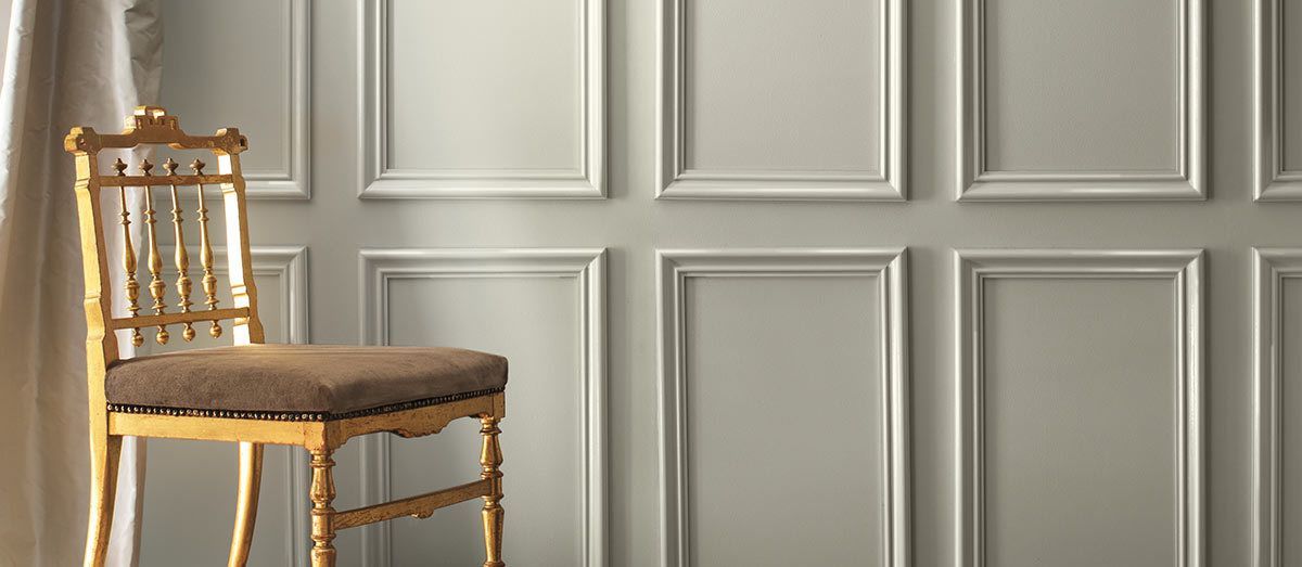 Gold chair with brown cushion against a gray wall with white rectangular frames, curtains on the left.