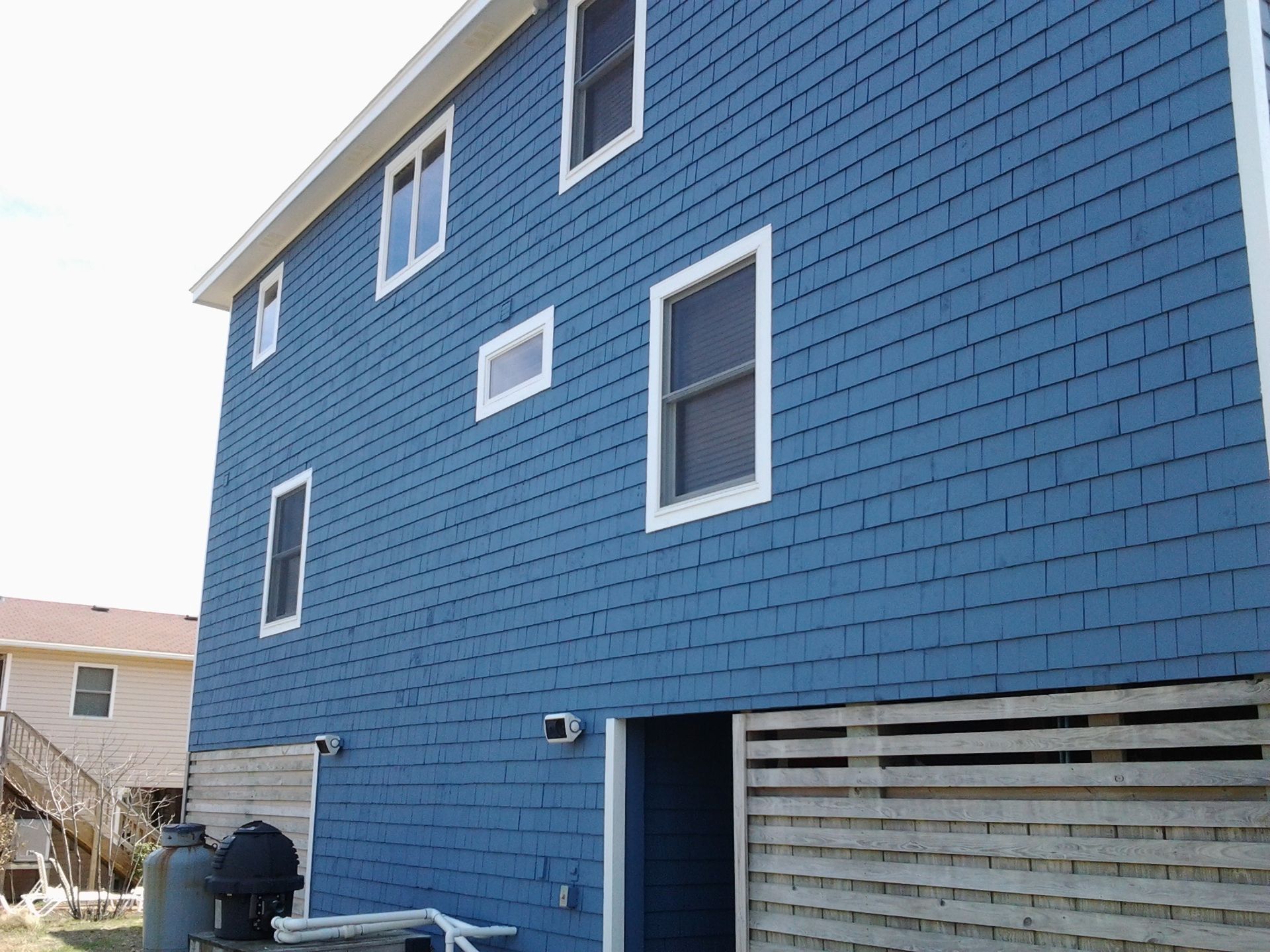 Blue shingled house exterior with white window frames and a slatted wooden fence.