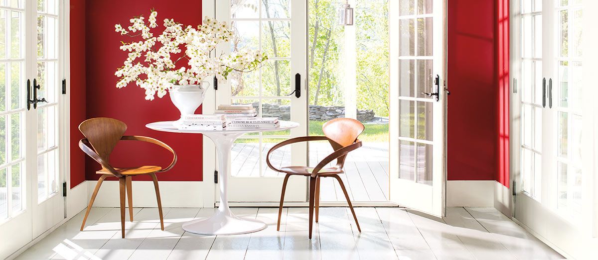 Red-walled room with white doors and a round table with flowers and wooden chairs.