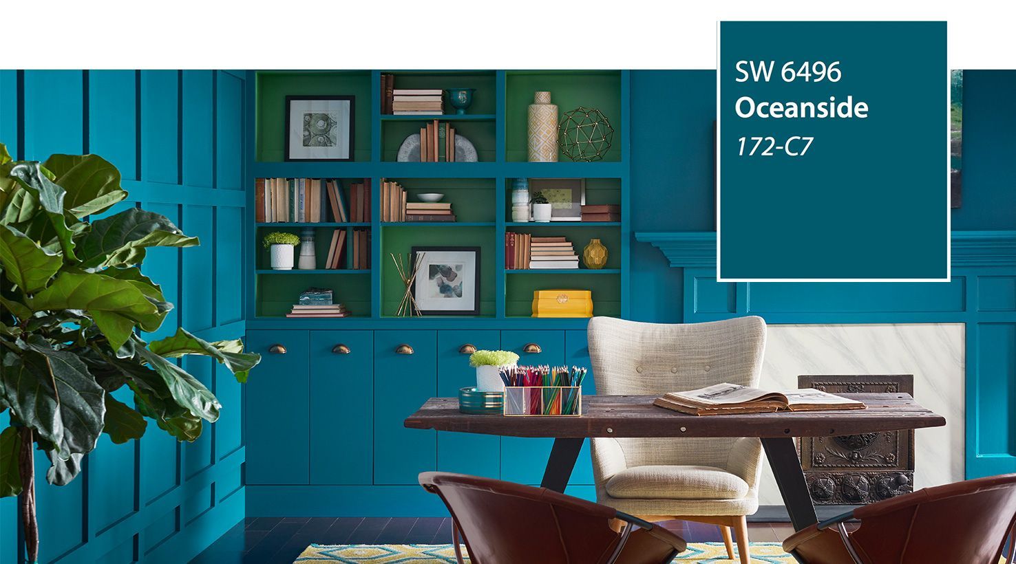 A home office with teal walls and green built-in shelves. A wooden desk and chairs sit in front.