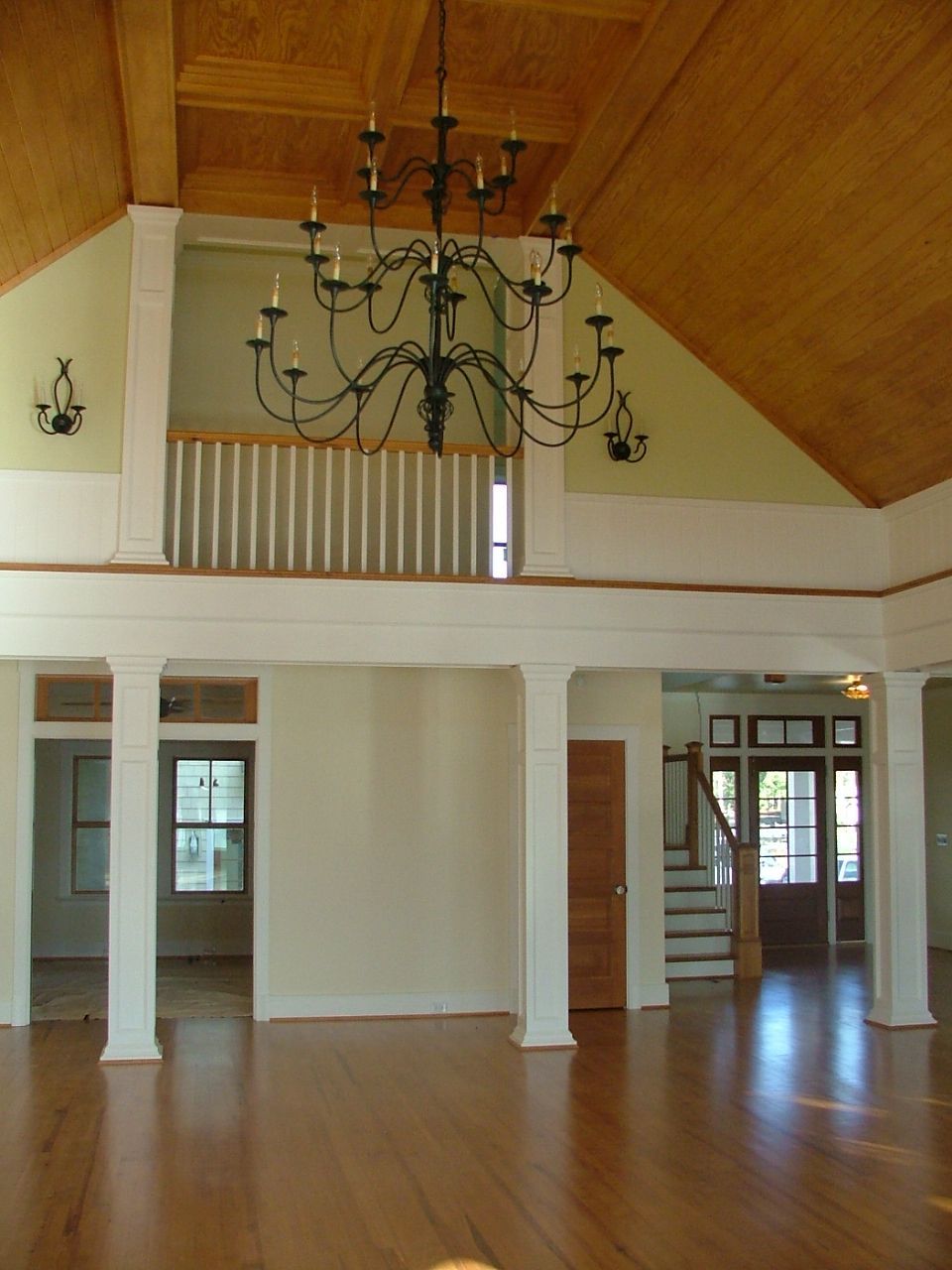 Spacious interior with hardwood floors, chandelier, and a second-floor balcony. Beige and white walls, wood ceiling.