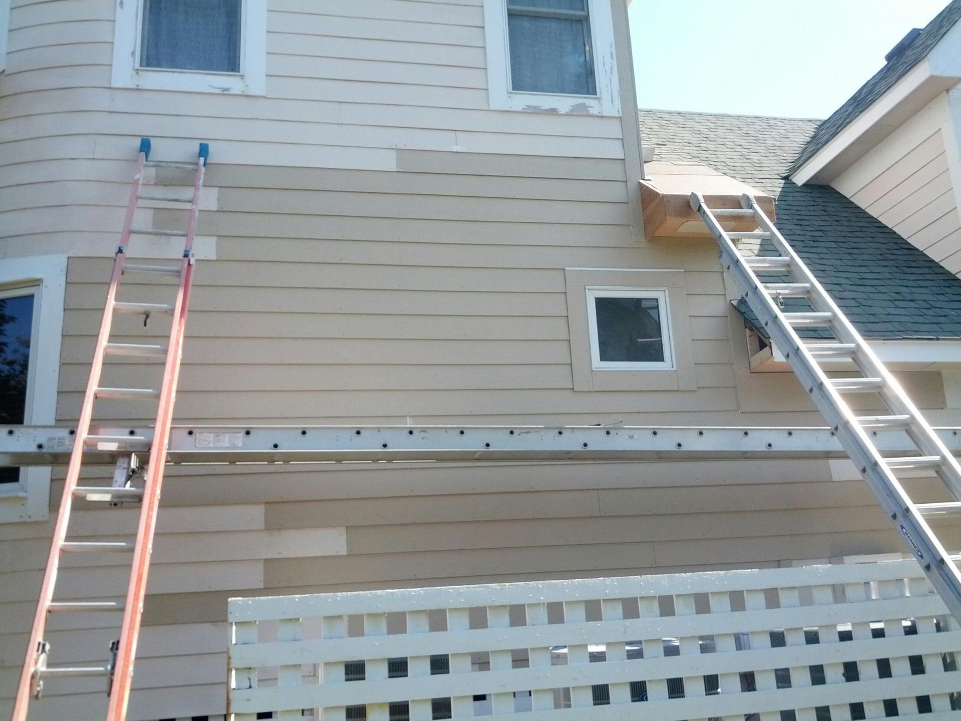 House exterior with ladders and scaffolding, showing siding repair and painting in progress.