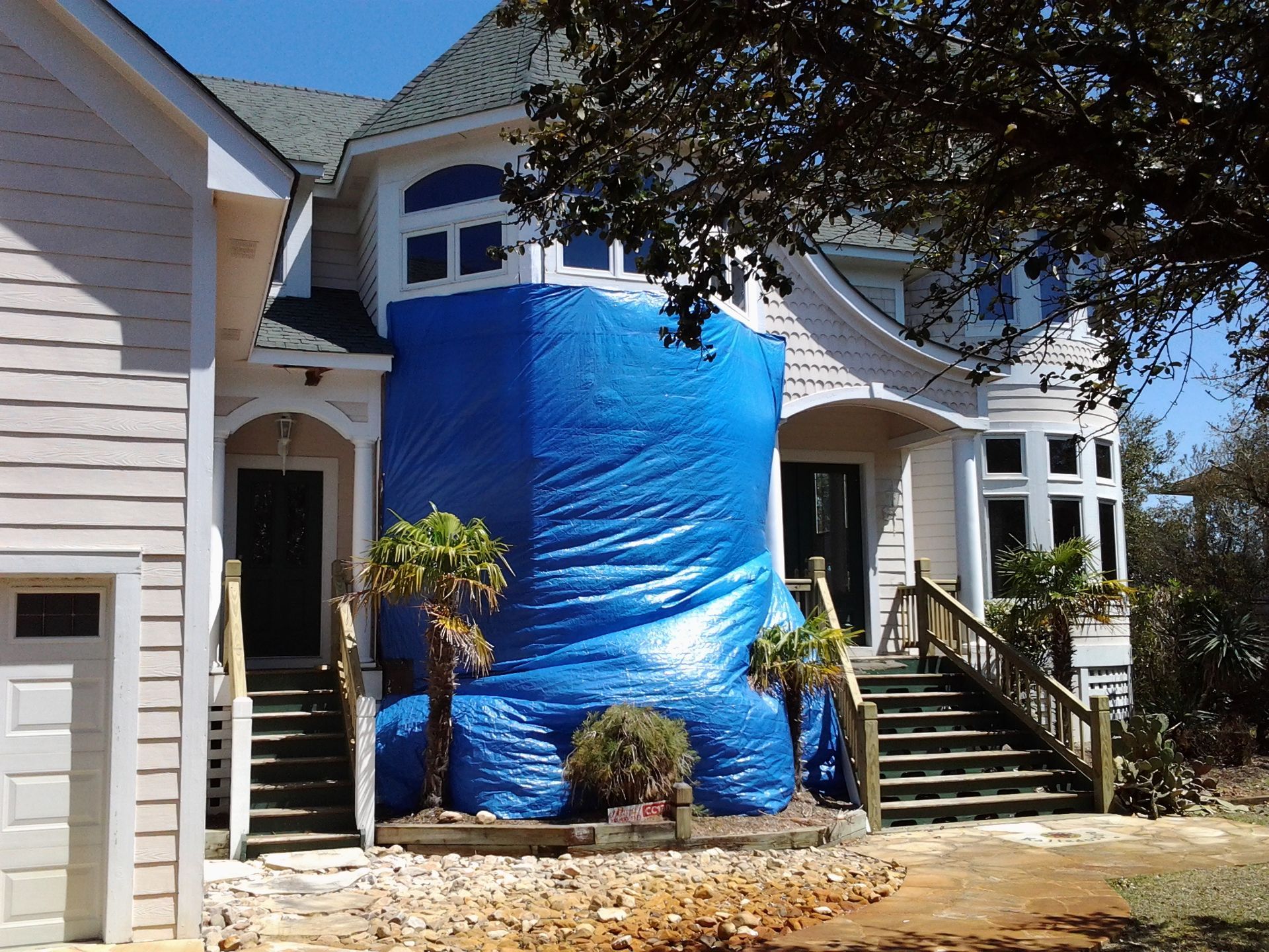 House exterior with blue tarp covering the front, a staircase, and a detached garage on the left.