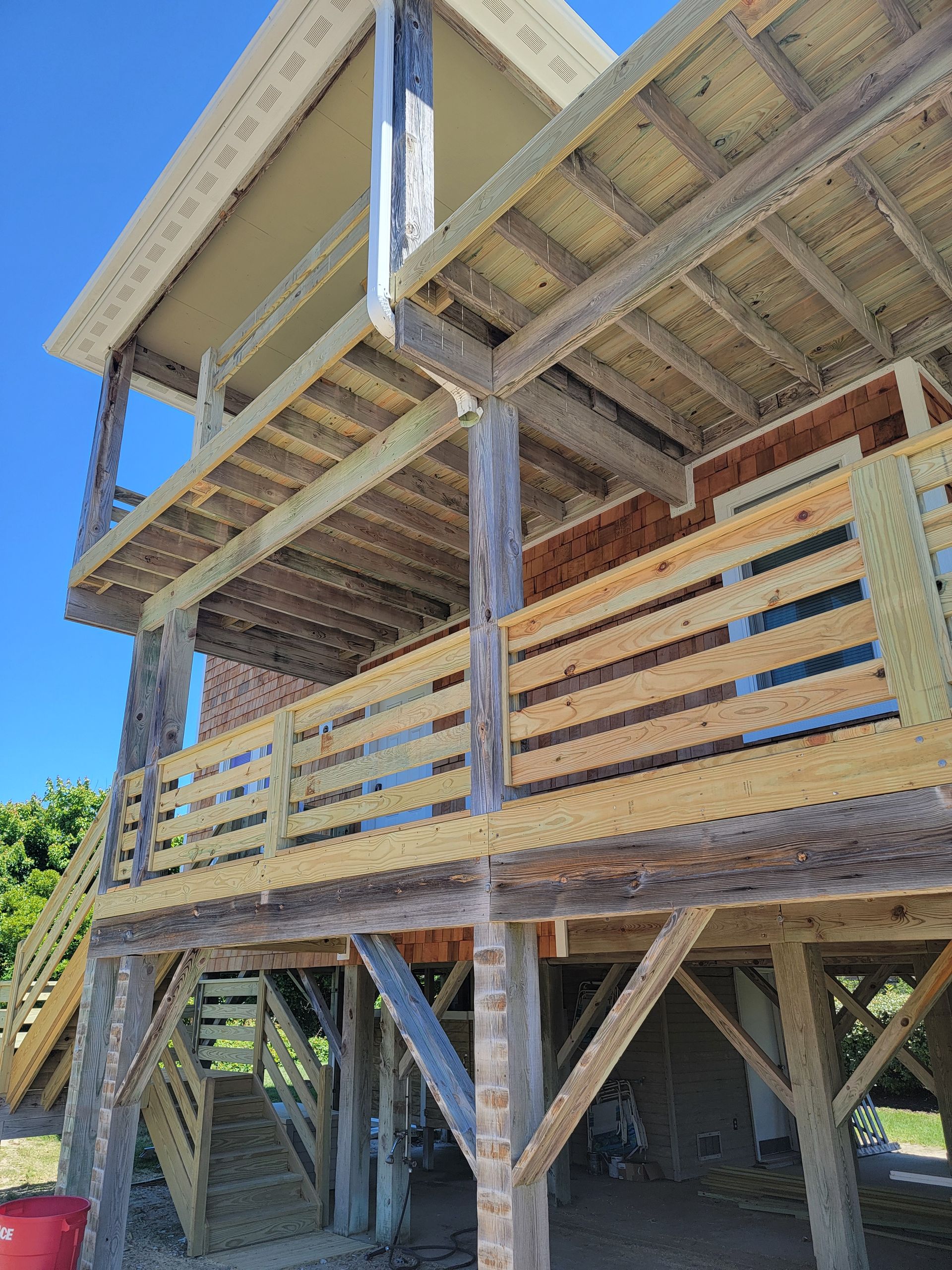 Wooden stilt house with multiple decks, featuring railings, support beams, and a clear blue sky.