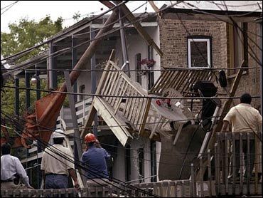 A partially collapsed house with people observing, debris, and power lines.