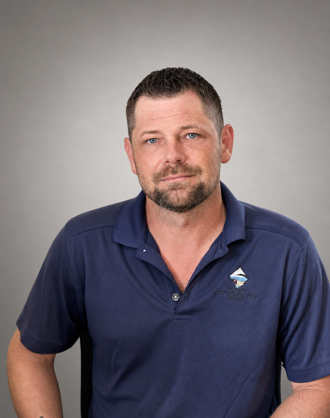Man with short brown hair and a goatee, wearing a blue shirt, smiling in front of an orange wall.