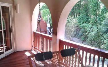 Covered porch with arches, a swinging bench, and a view of greenery.