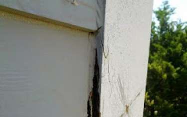 Corner of a white building with vertical cracks and discoloration. Brownish staining visible.