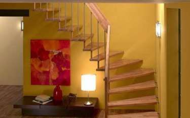 Wooden spiral staircase with metal railing on yellow wall.