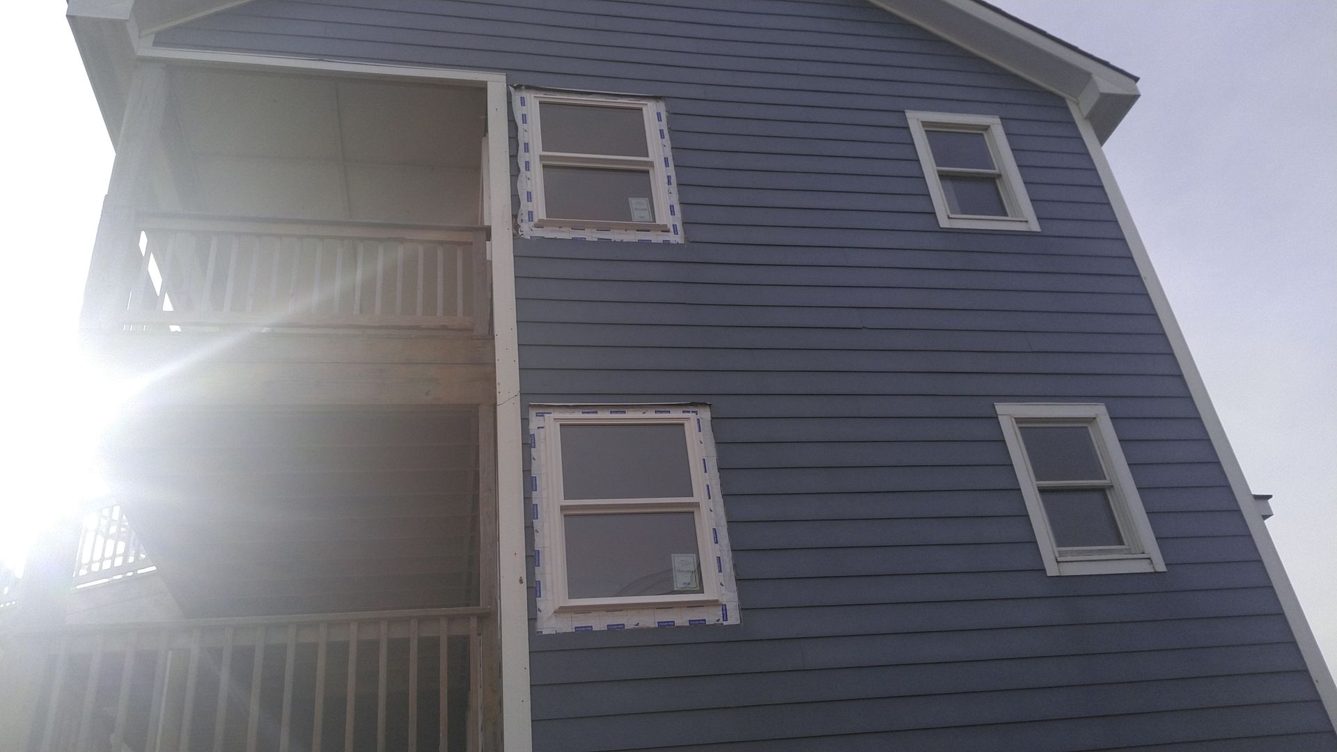 Blue-sided building with two-story balcony, several windows, and sunlight obscuring part of the image.