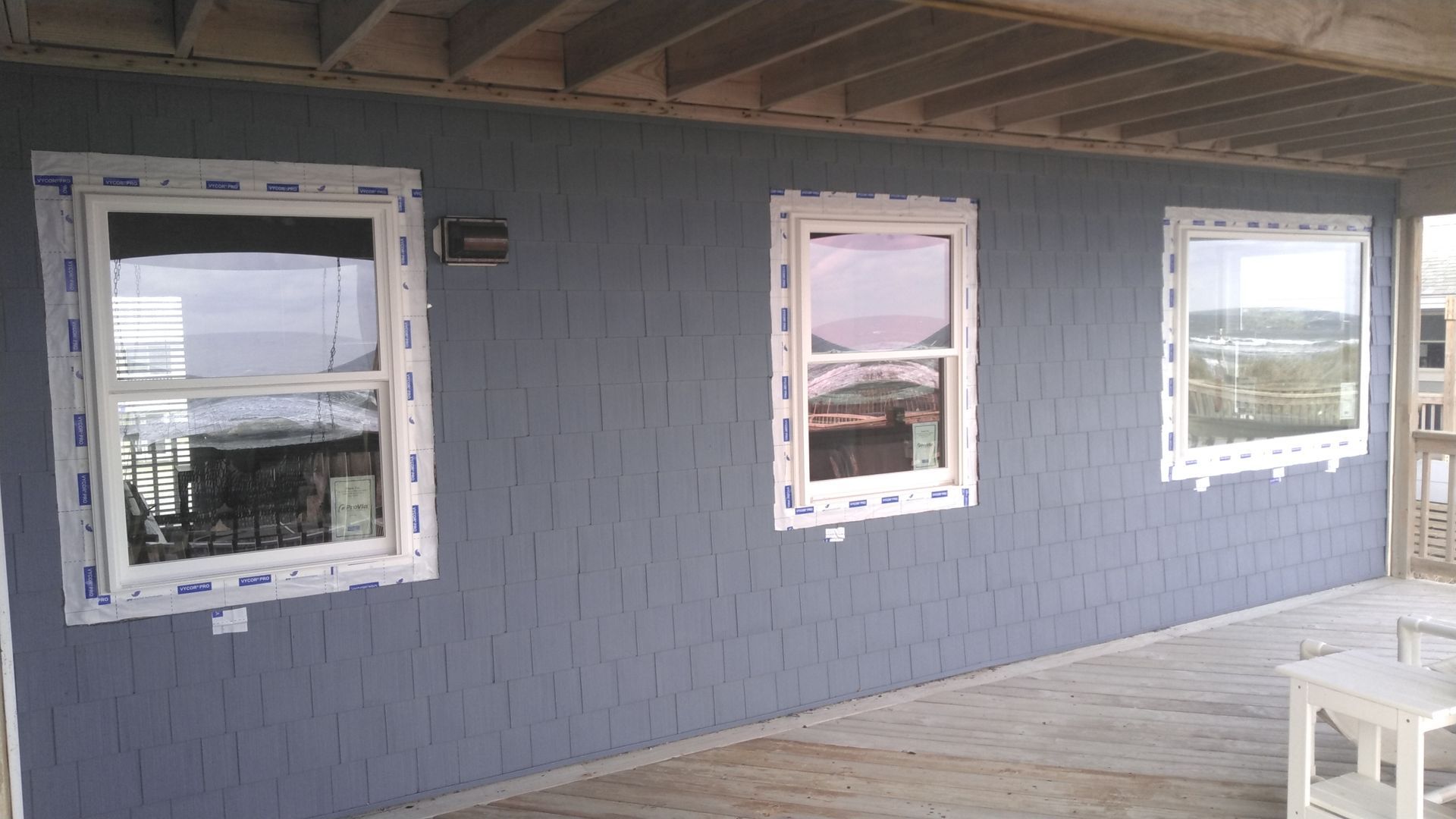 Three windows with white frames on a blue-gray exterior wall under a wooden roof.