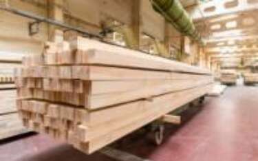 Stack of lumber on a wheeled cart in a factory.