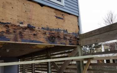 Damaged house siding and wood framing, showing water damage, next to a wooden deck.