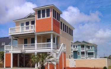 Beach house with orange and light peach exterior, white balconies, and a tower.