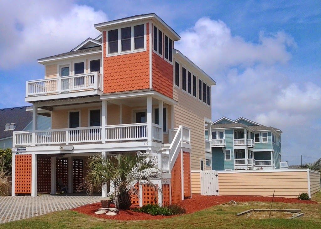 Two-story beach house with orange accents, white balconies, and a smaller light blue house in the background.