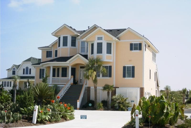 Large, yellow beach house with multiple stories, white trim, and a black roof.