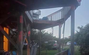 Wooden deck elevated on supports, overlooking a yard with parked cars.