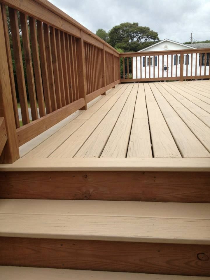 Wooden deck with steps, railings, and light-colored planks. Cloudy sky, house visible in the background.