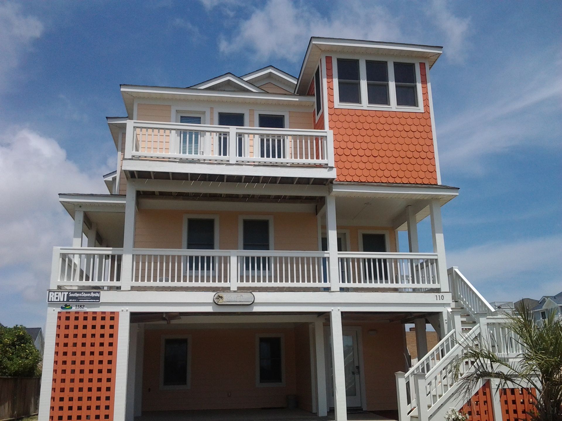 Two-story beach house with orange accents, balconies, and a screened tower against a blue sky.