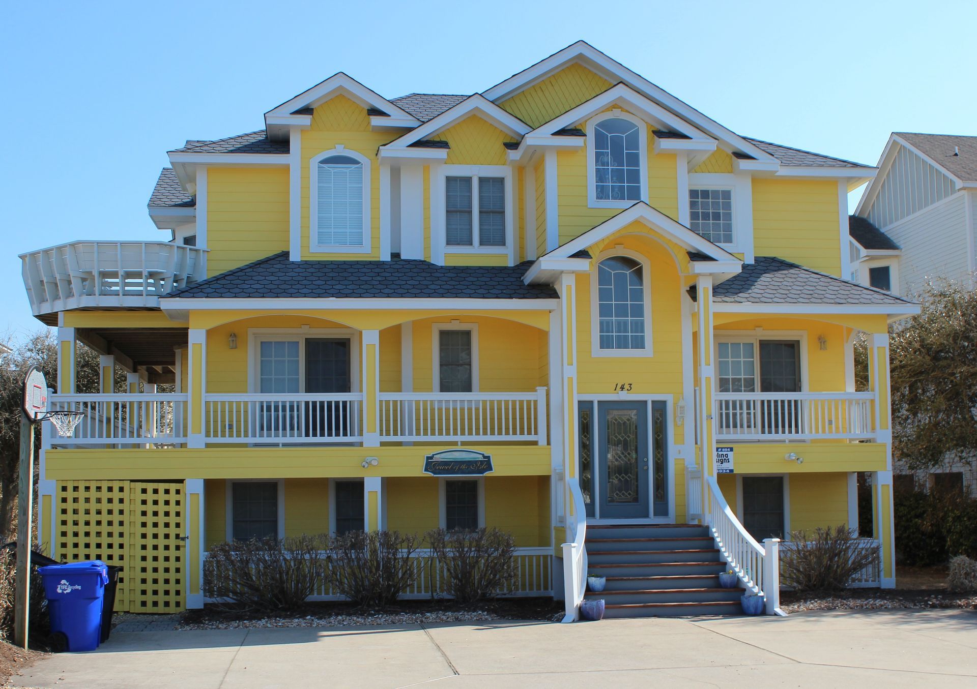 Yellow multi-story beach house with white trim, porch, and a blue sky.