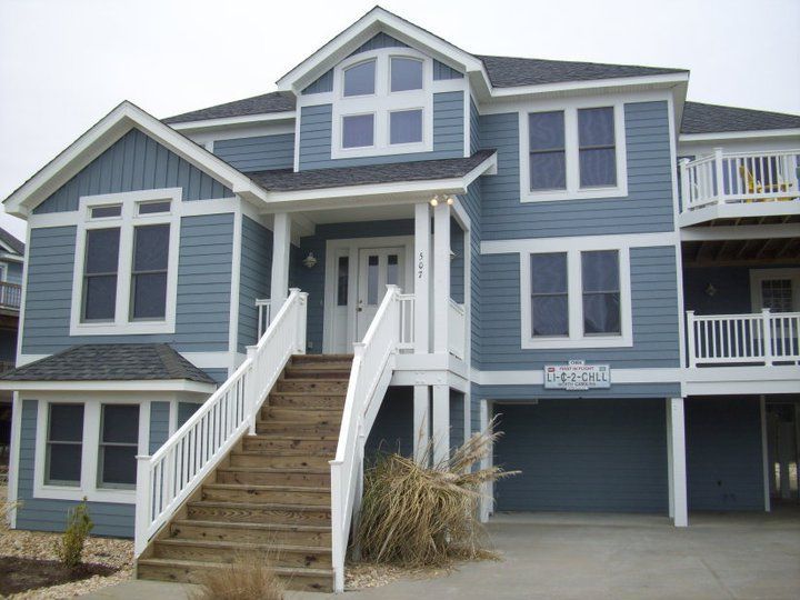 Two-story blue beach house with white trim, stairs, and windows.