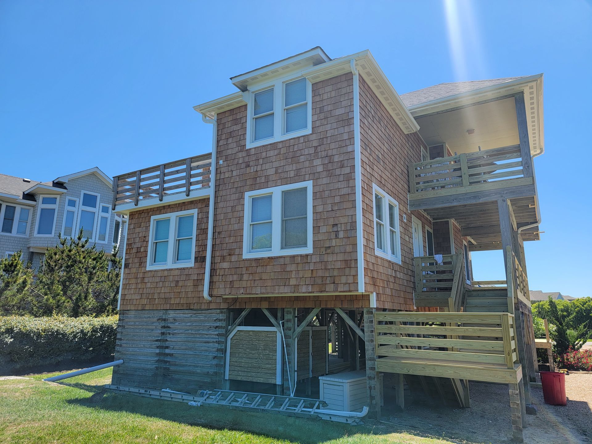 Two-story beach house on pilings with wooden deck and cedar shake siding under a blue sky.