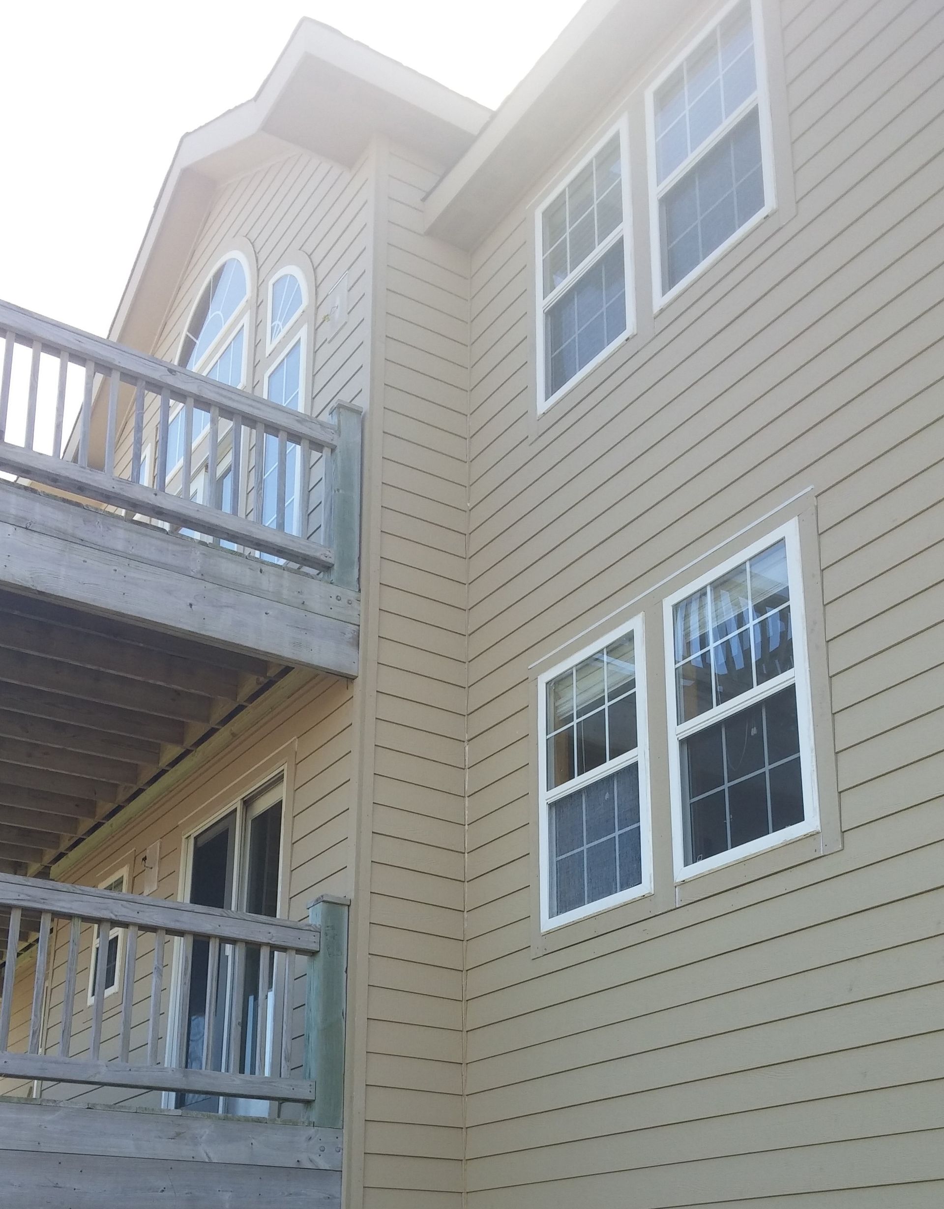 Tan house exterior with deck and white-framed windows.