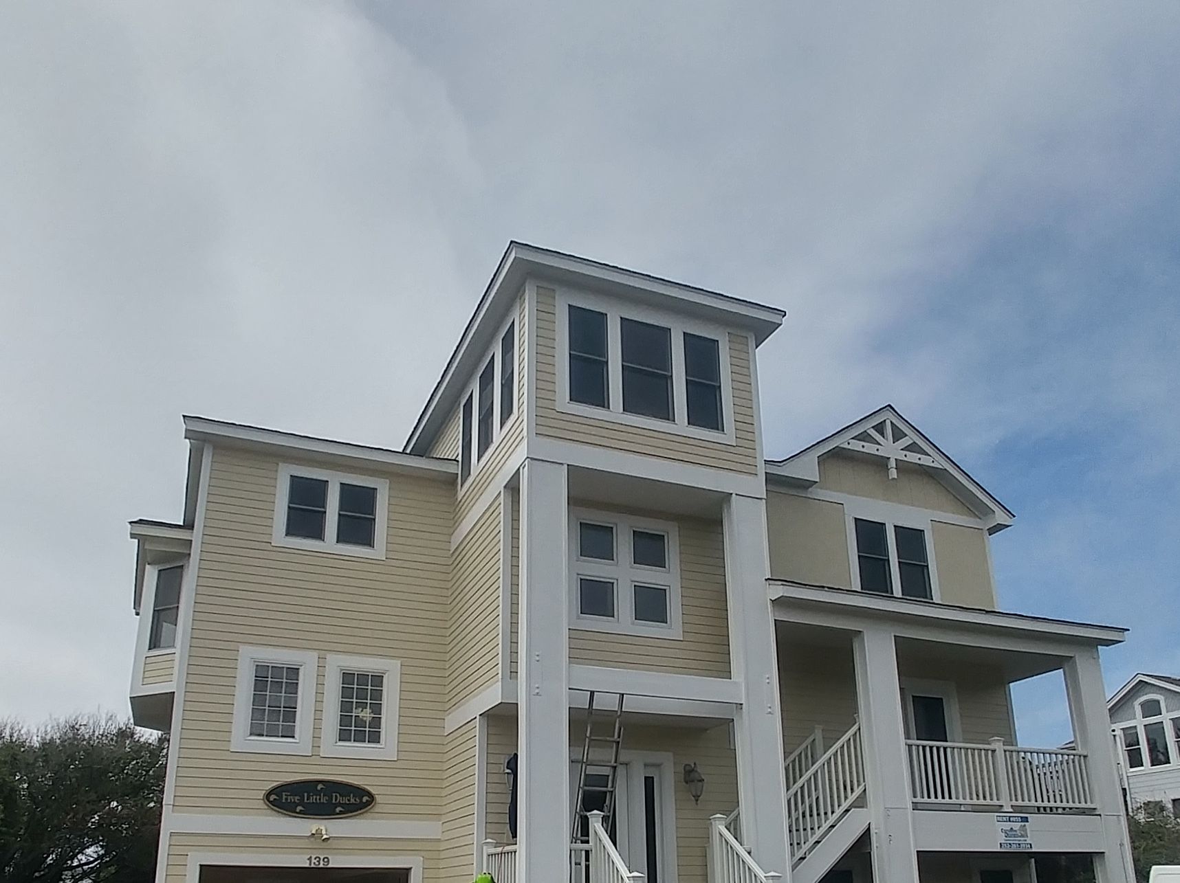 Beige two-story house with dark shutters, white trim, and a porch under a cloudy sky.