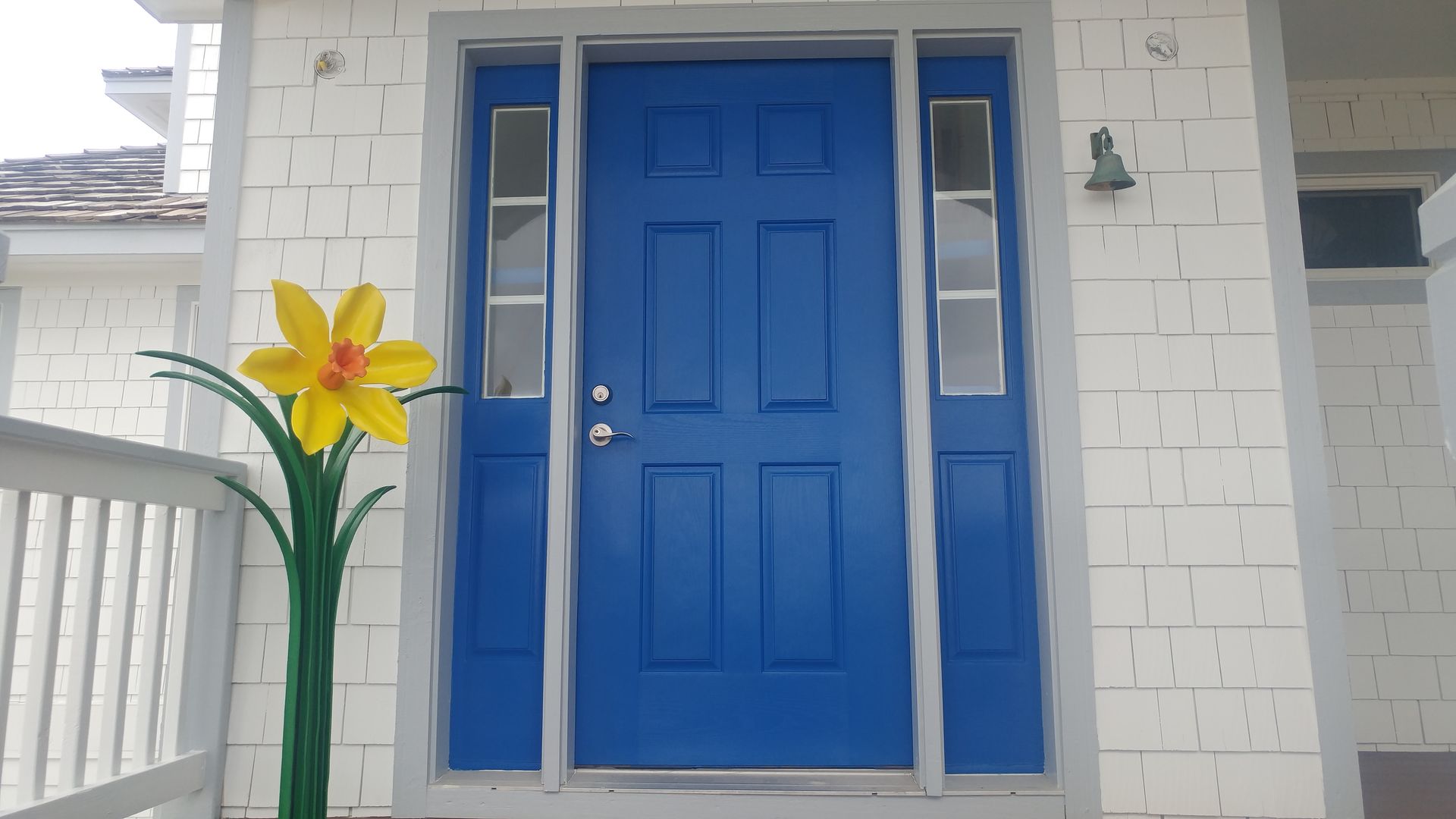 Blue front door with sidelights, white siding, and a large yellow daffodil.