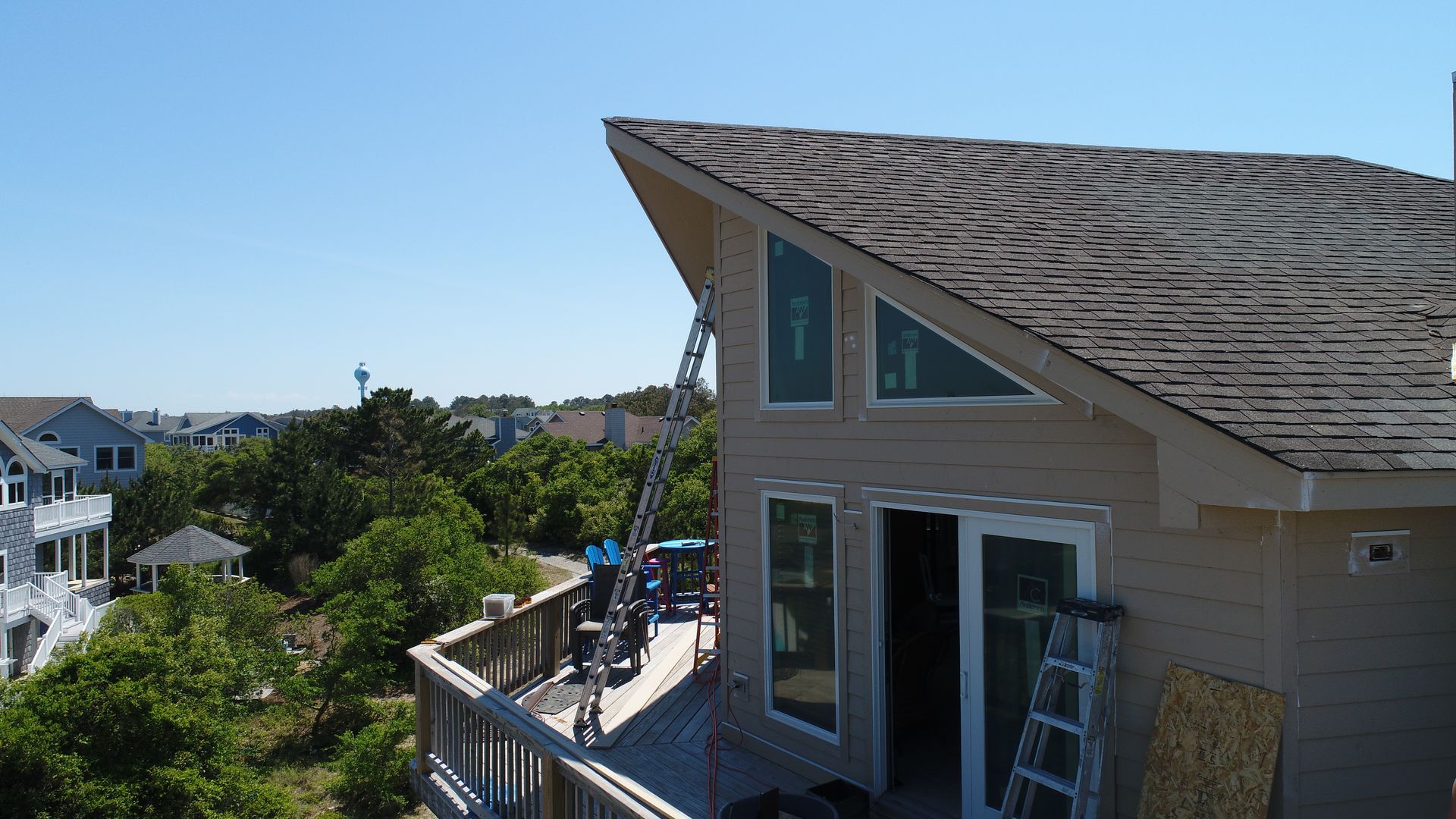 House exterior with angled roof and large windows, workers on deck, blue sky.