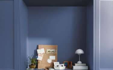 Blue built-in niche with desk, corkboard, lamp, and small objects.
