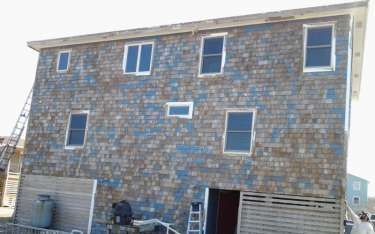 Two-story building with weathered blue-brown shingles, multiple windows, and a ladder leaning against it.