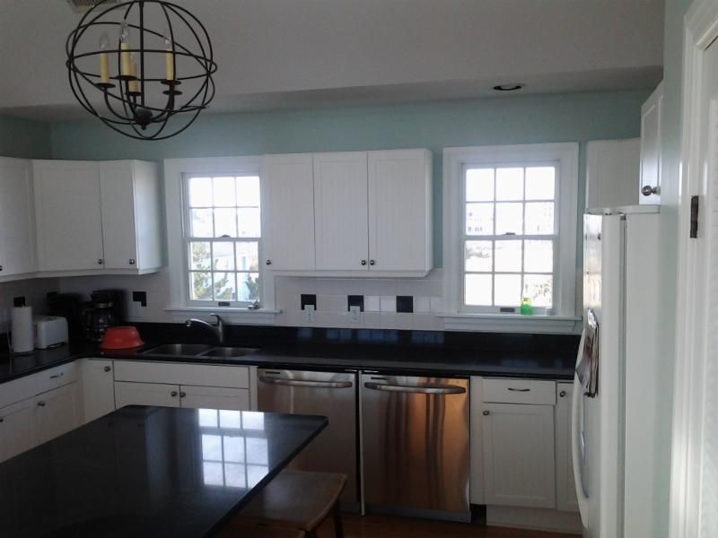 White kitchen with black countertops, stainless steel appliances, and a hanging orb light fixture.
