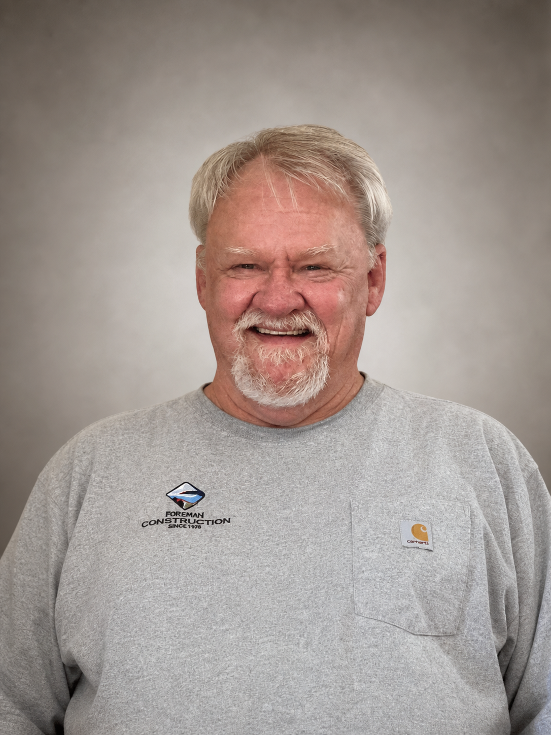 Man with graying hair and beard in front of a blue background, wearing a white shirt.
