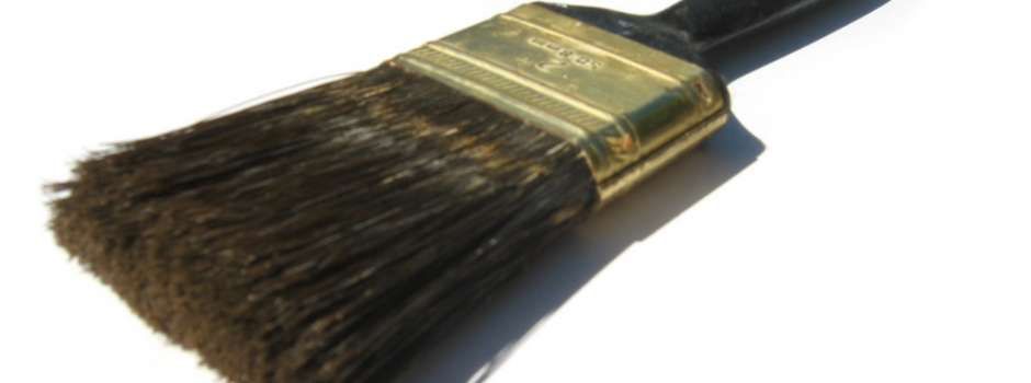 Close-up of a paint brush with dark bristles, a gold ferrule, and a black handle, resting on white.
