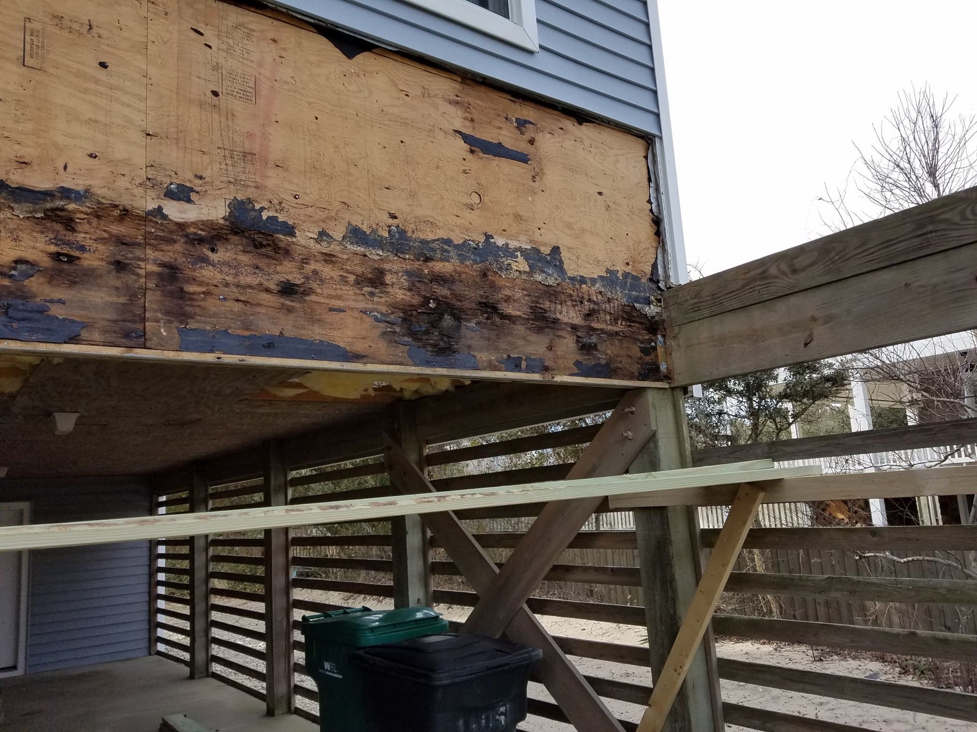 Exterior house wall with damaged wood, adjacent to a deck.