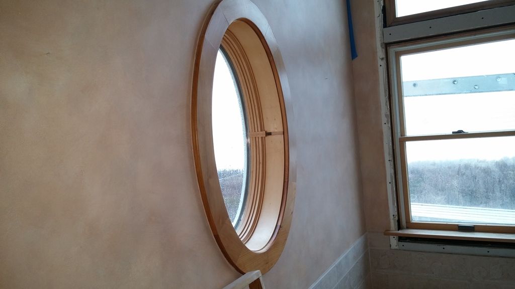 Oval window with wooden frame on a light-colored wall, next to a rectangular window.