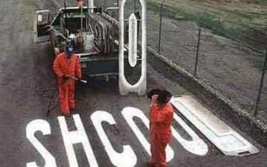 Two workers paint a large clip on asphalt next to the word