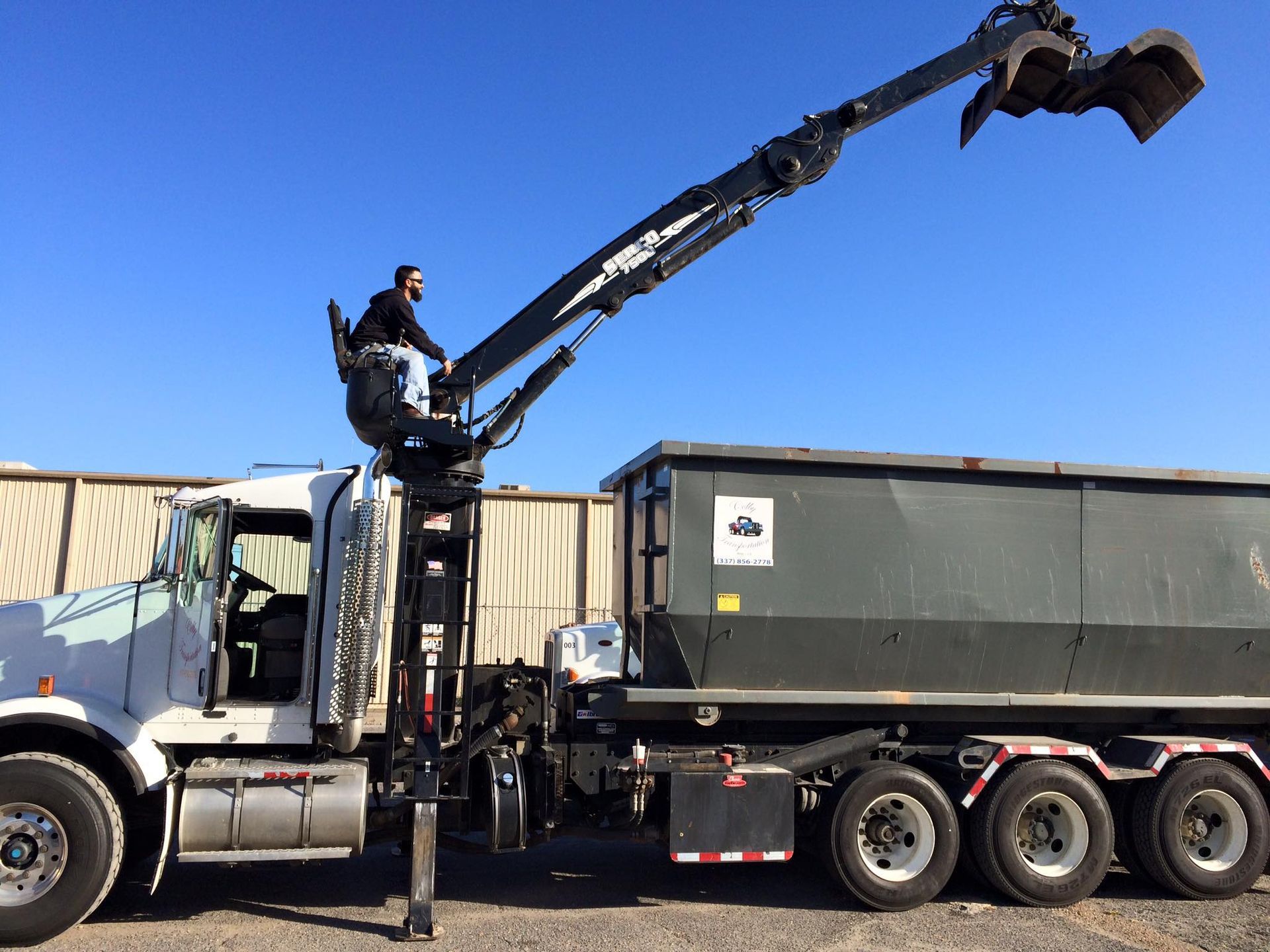 Truck with crane arm holding large claw, operator in seat, blue sky.