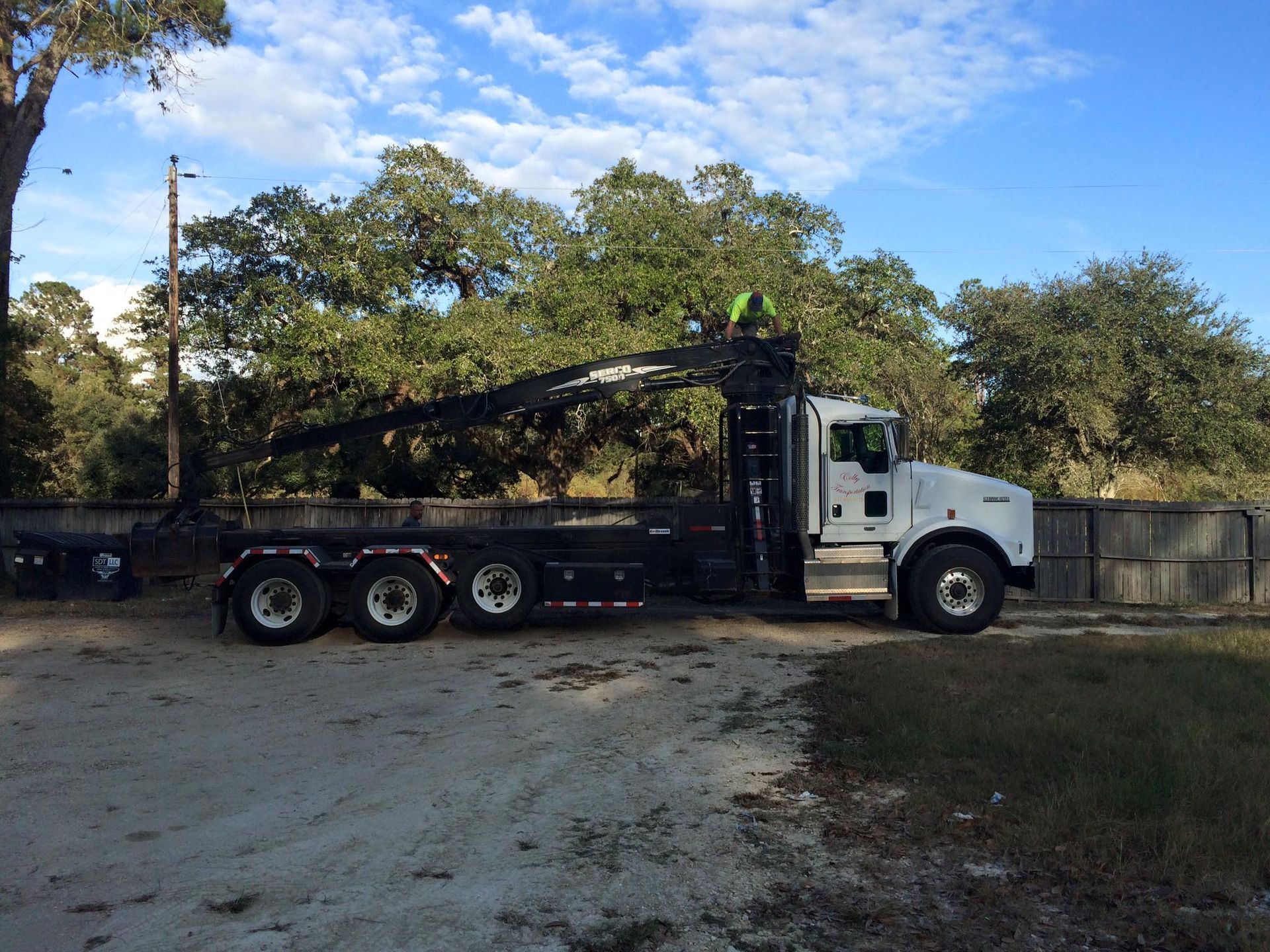 White dump truck with a raised arm, tree trimming in progress.