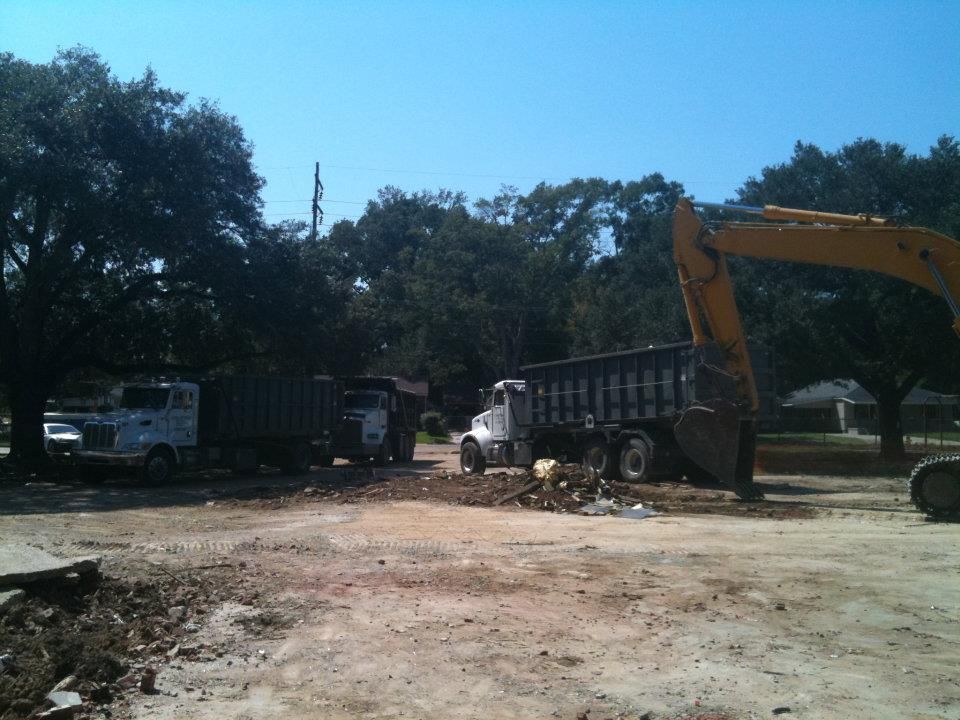 Construction site: Excavator loading dirt into dump trucks under a bright blue sky.