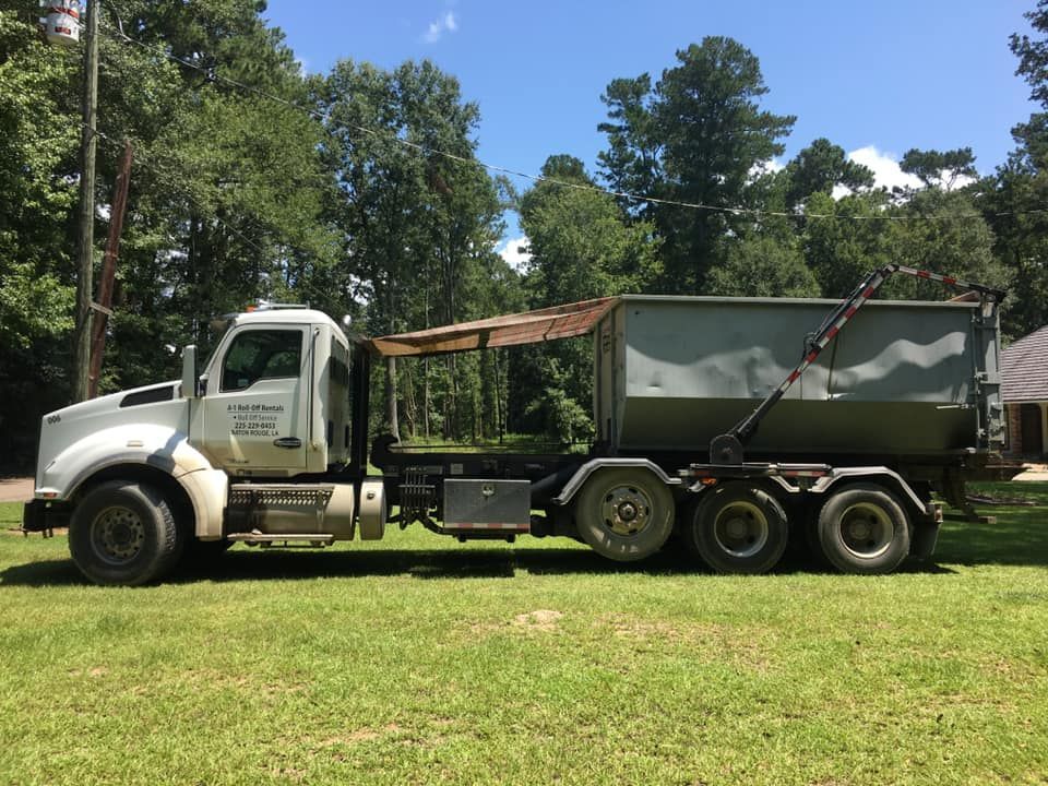 White dump truck on grass, gray container. Sunny day, trees in background.