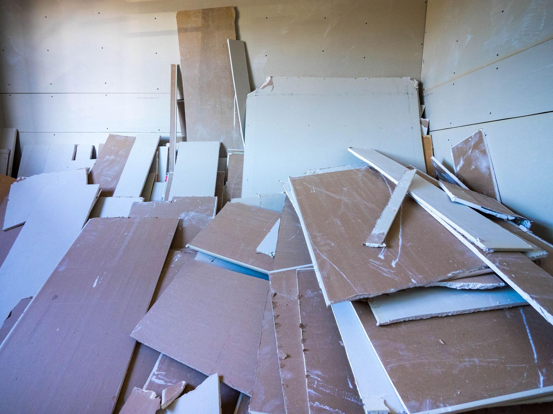 Pile of broken cardboard and drywall debris in an empty room with white walls.