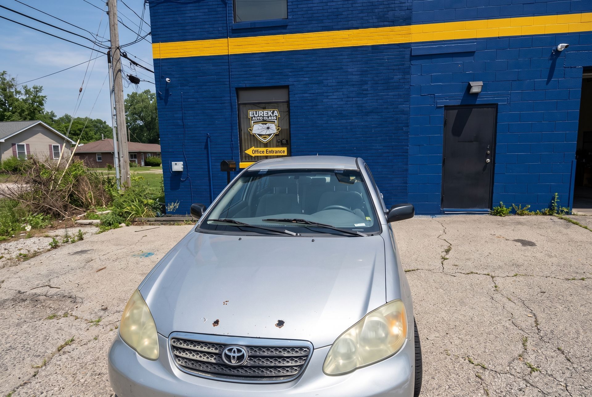 Silver car parked in front of a blue building with a yellow stripe and a black door