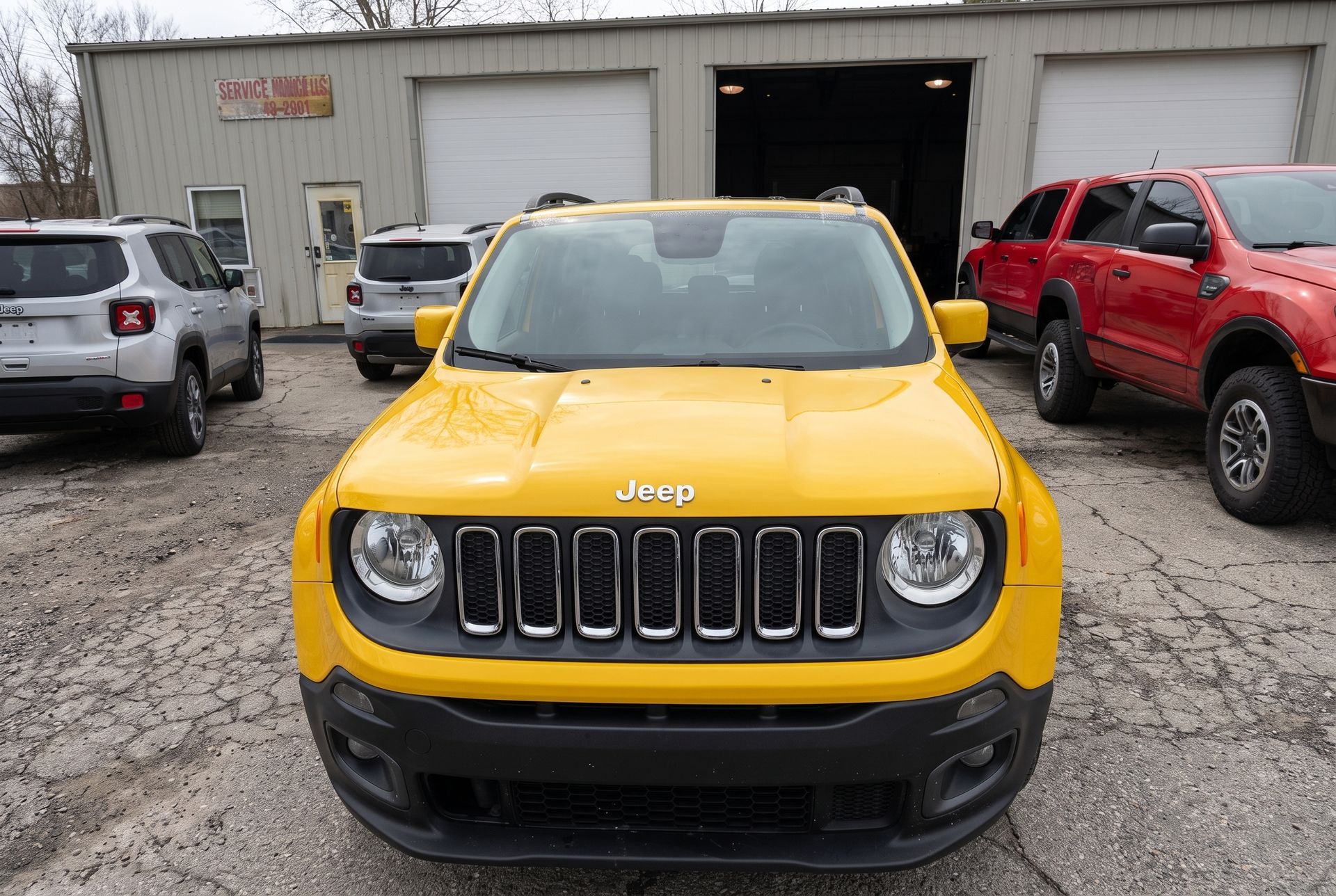 Yellow Jeep SUV parked in front of a garage with other vehicles nearby