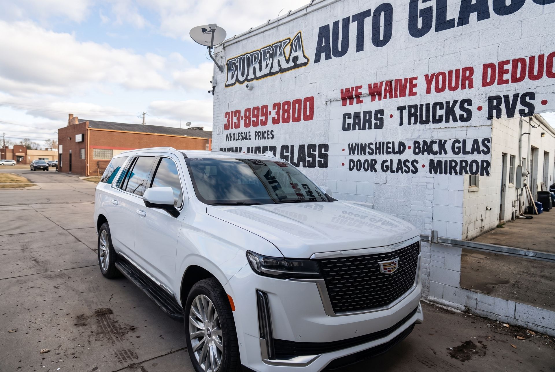 White SUV parked beside an auto glass shop mural on a cloudy street.