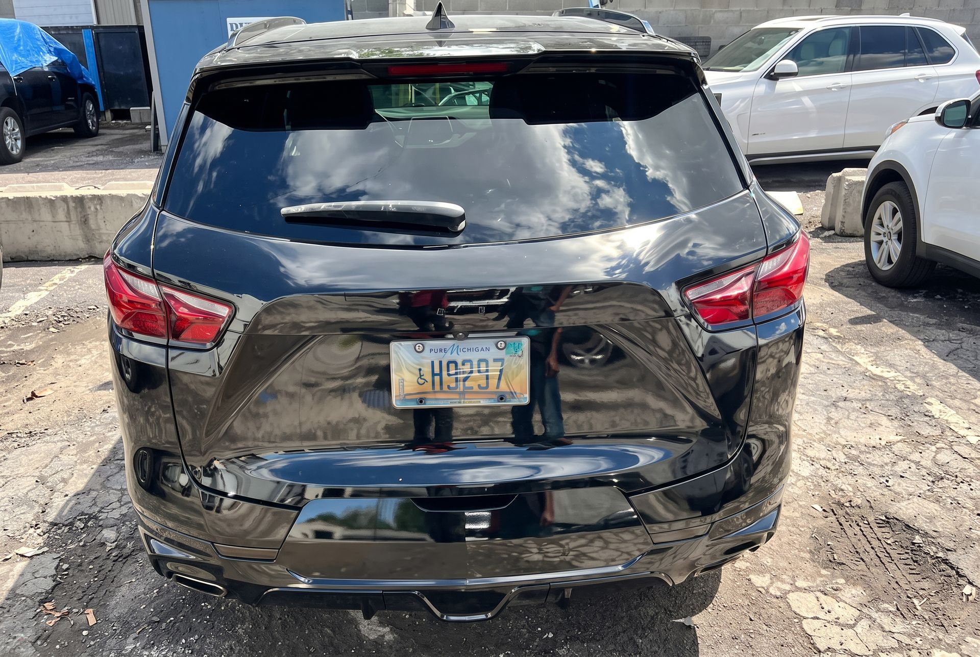 Rear view of a damaged black SUV with a dented liftgate and broken rear bumper in a parking lot