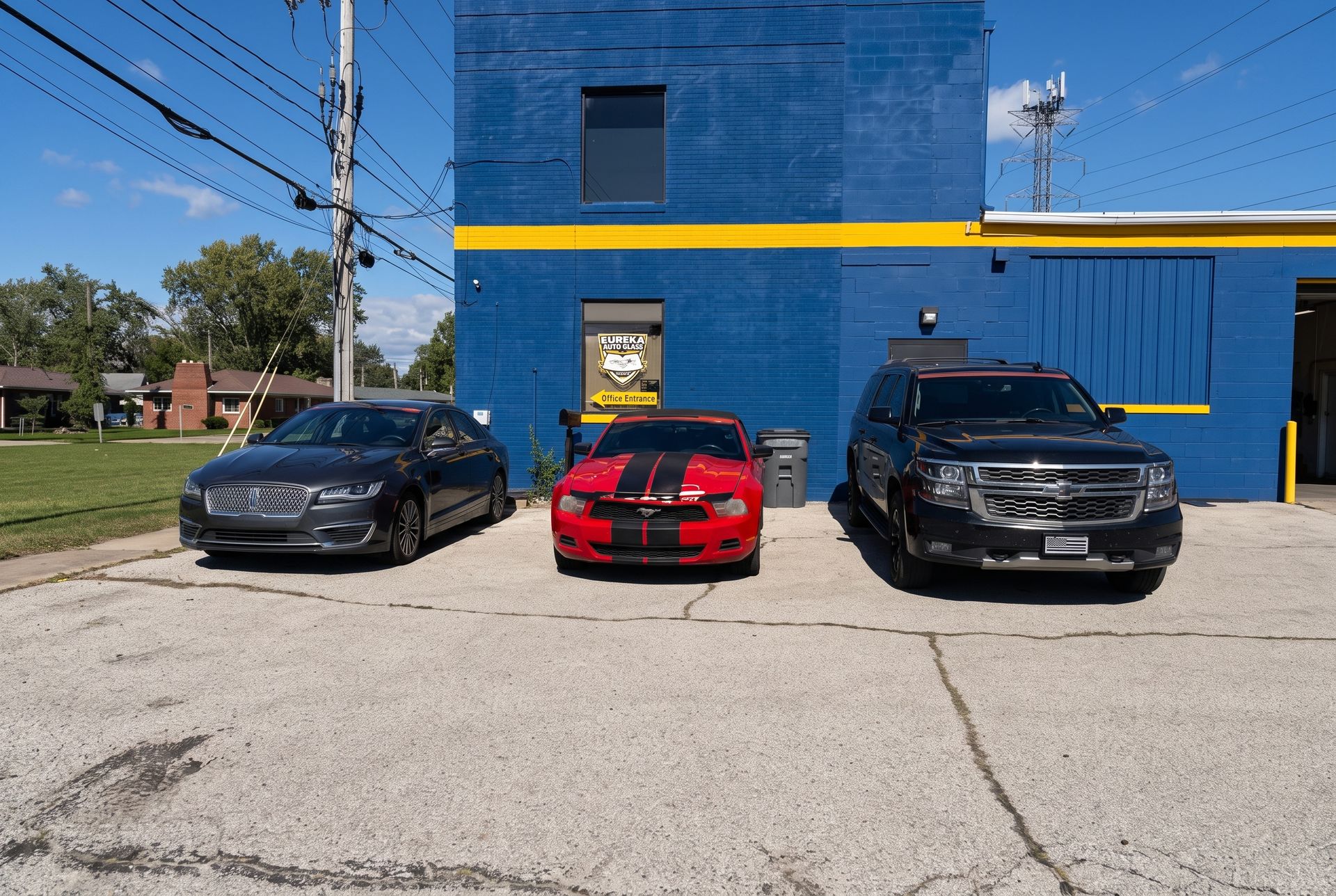 Three parked cars in front of a blue building with a yellow stripe on a sunny day