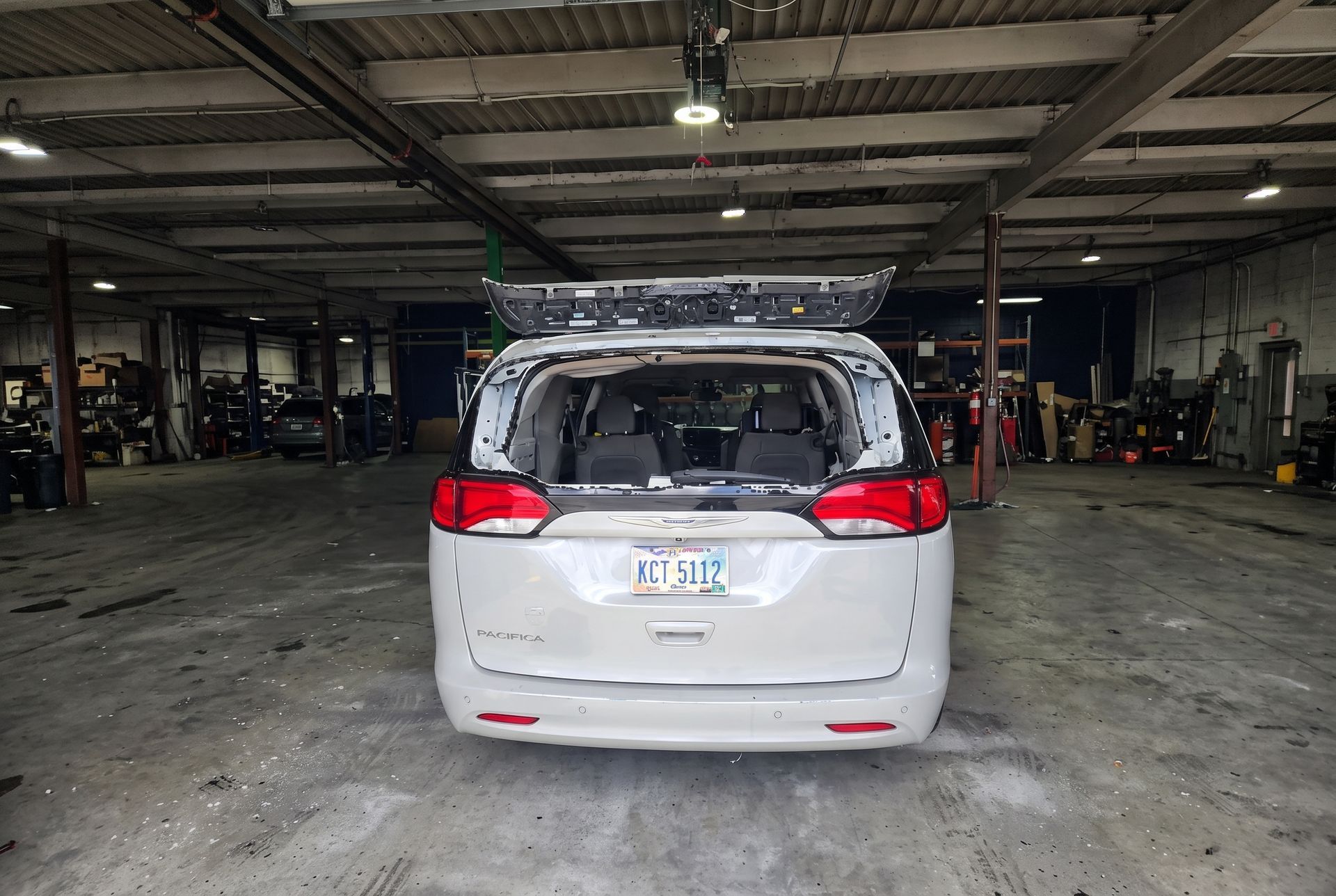 Silver minivan parked in a dim auto garage, viewed from the rear.